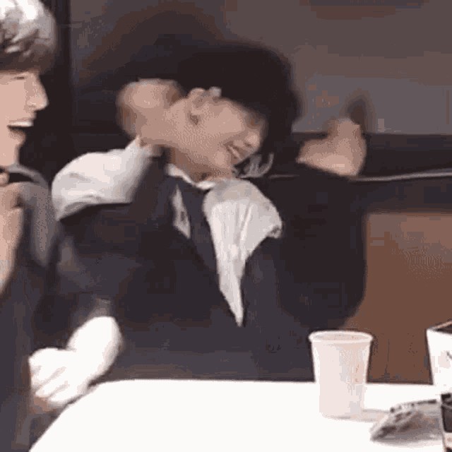 a man in a suit and tie is sitting at a table with his arms outstretched and laughing .