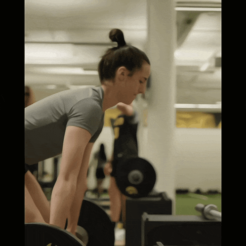 a woman in a gray shirt is lifting a barbell in a gym