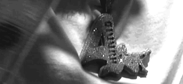 a black and white photo of a person holding a pendant that says ' a ' on it