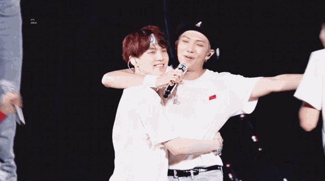 a man holding a microphone while hugging another man with red hair