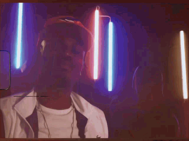 a man in a red hat stands in a dark room surrounded by neon lights