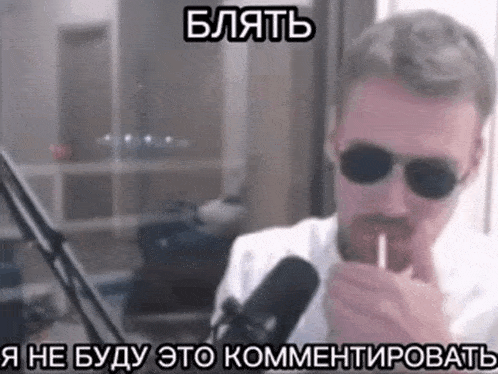 a man wearing sunglasses smoking a cigarette in front of a microphone
