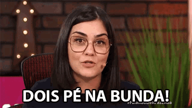a woman wearing glasses is sitting in a chair with a microphone in her mouth and says dois pe na bunda !