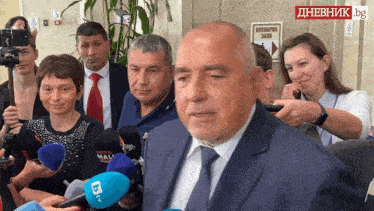 a man in a suit and tie is surrounded by reporters and a sign that says dnevnik bg