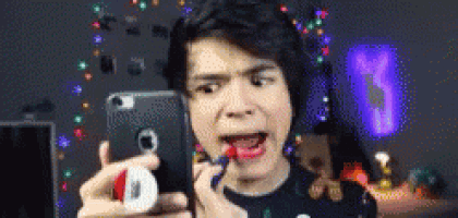 a man is applying lipstick to his lips while taking a selfie with his phone .