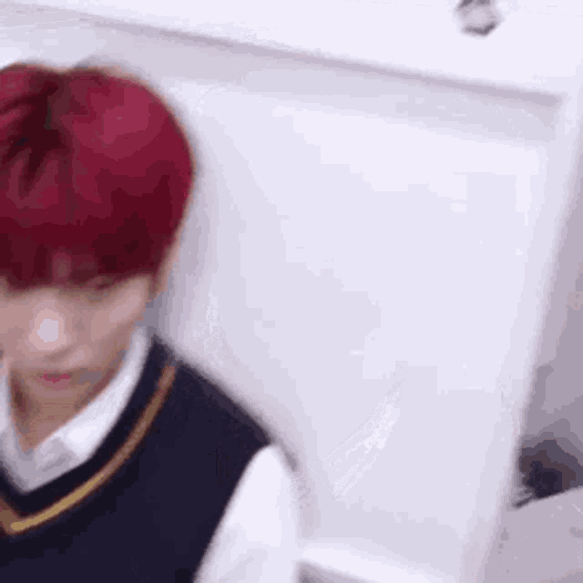 a young man with red hair is sitting in front of a white wall in a room .