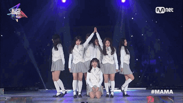a group of girls are kneeling down on a stage with a mnet logo behind them
