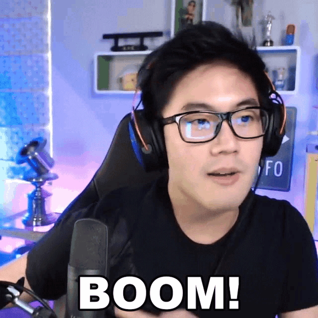 a man wearing headphones and glasses says boom in front of a microphone