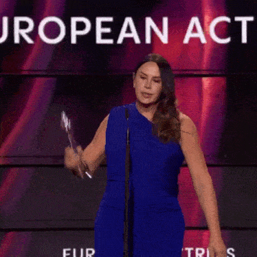 a woman in a blue dress is holding up a trophy in front of a sign that says european act