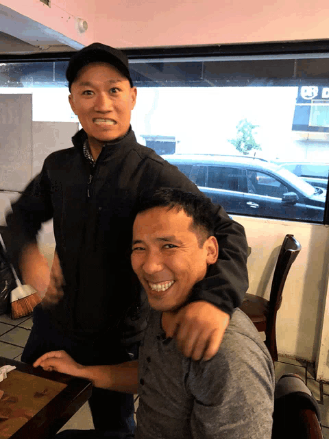 two men are posing for a picture in front of a window that has a sign that says ' a ' on it
