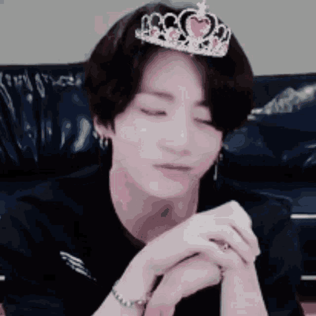 a young man wearing a tiara on his head is sitting on a couch with his eyes closed .