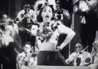 a black and white photo of a woman dancing in front of a brass band .