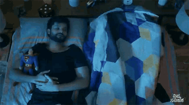 a man is laying in bed with a superman stuffed animal