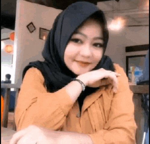 a woman wearing a hijab and a yellow shirt is sitting at a table in a restaurant .