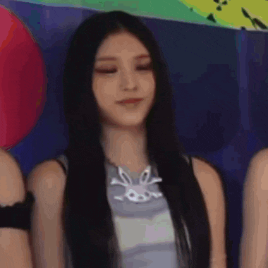 a woman with long black hair is sitting in front of a group of people and smiling .