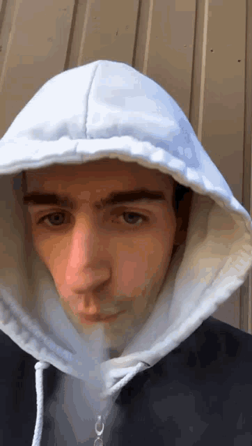 a man wearing a white hoodie is smoking an electronic cigarette