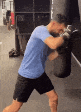 a man in a blue shirt is punching a boxing bag