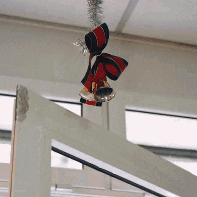 a pair of bells hanging from a ceiling with a red and black bow