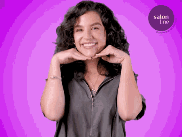 a woman with curly hair is smiling in front of a purple background with a salon line logo