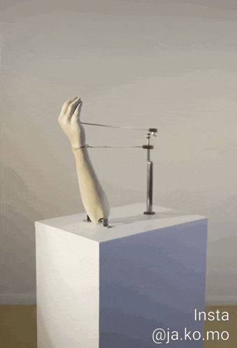 a statue of a hand on a white pedestal with insta @ja.ko.mo written below it