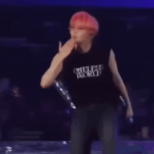 a man with red hair is standing on a stage holding a microphone and wearing a black shirt that says timeless world .