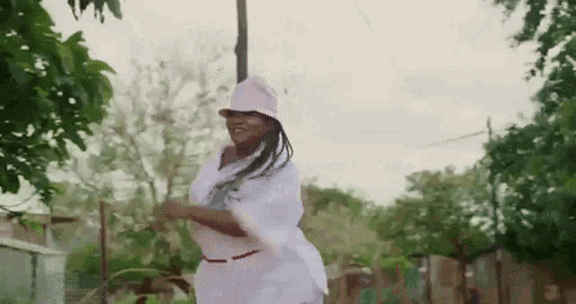 a woman wearing a pink hat and a white dress is dancing in a park .