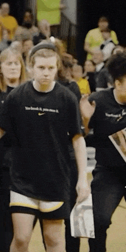 a woman wearing a black nike t-shirt stands in front of a crowd .