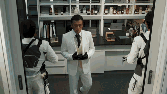 a man in a white suit stands in front of a shelf with bottles on it
