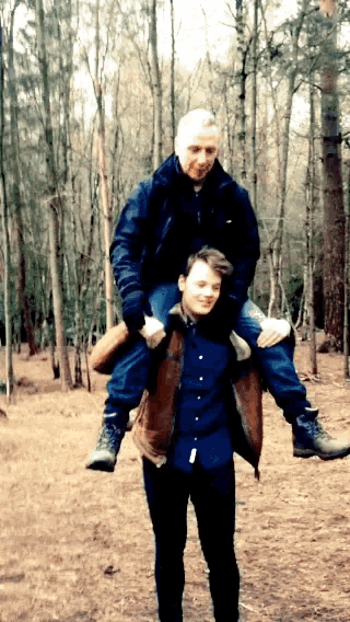 a man is carrying another man on his shoulders in a forest