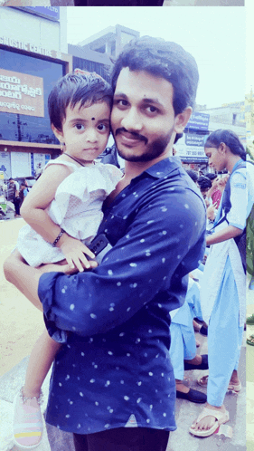 a man in a blue shirt holds a little girl in front of a building that says ' telugu cinema '