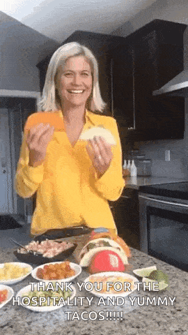 a woman in a yellow shirt is holding a taco in her hands and smiling .