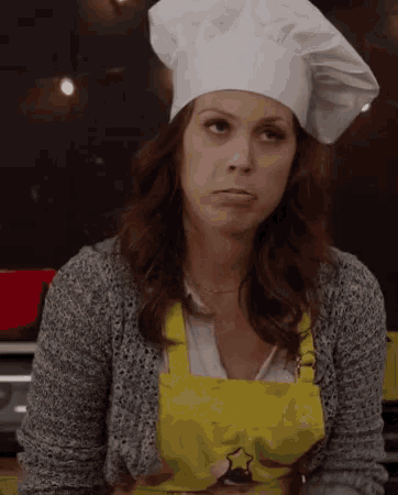 a woman wearing a chef 's hat and an apron is making a face .