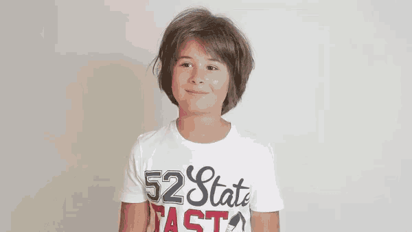 a young boy wearing a white t-shirt with the number 52 on it is making a funny face .