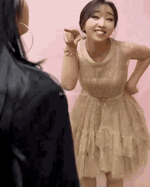 a woman in a gold dress is pointing to another woman