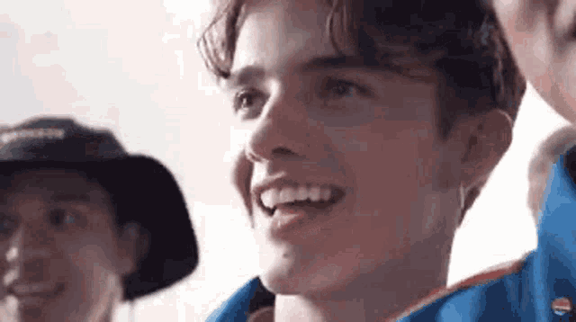 a young man is smiling and looking at the camera while standing next to a group of people .
