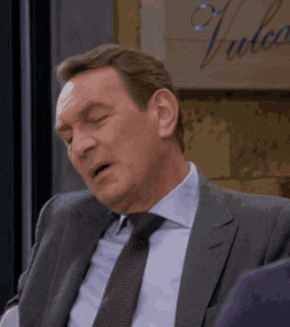 a man in a suit and tie is sitting in front of a sign that says ' yule ' on it