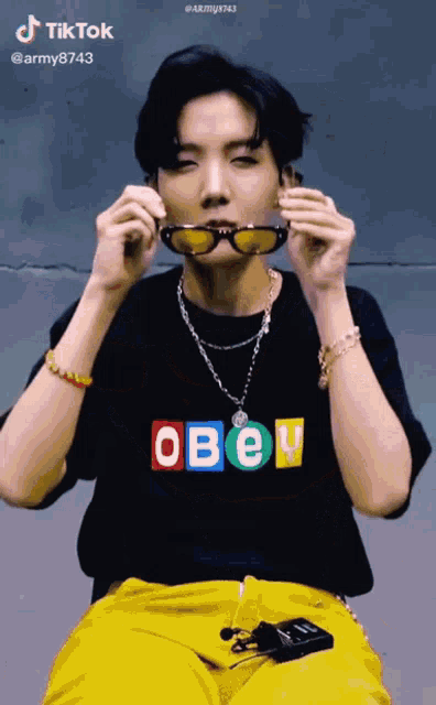 a man wearing a black shirt that says obey is holding sunglasses in his mouth