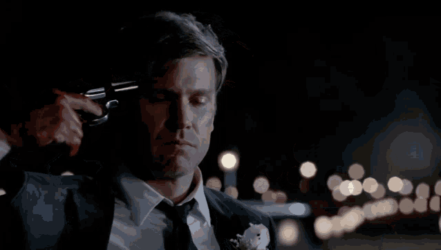 a man in a suit and tie has a bloody hand pointing a gun at his head