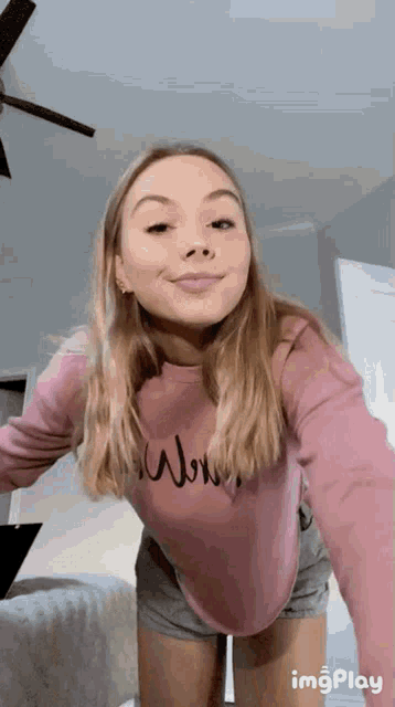 a woman in a pink sweater and shorts is taking a selfie in a bedroom .