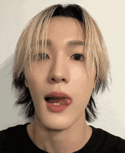 a young man with blonde hair is sticking his tongue out while wearing a black shirt .