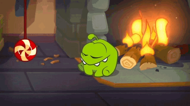 a green cartoon character is sitting in front of a fire