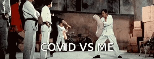 a group of people are standing around a man in a karate uniform who is kicking a pillow .