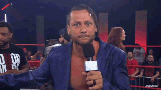 a man in a wrestling ring holds a microphone and says stupid in pink letters
