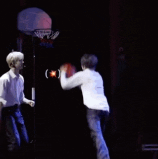 two men are playing basketball on a stage and one of them is jumping to catch the ball .