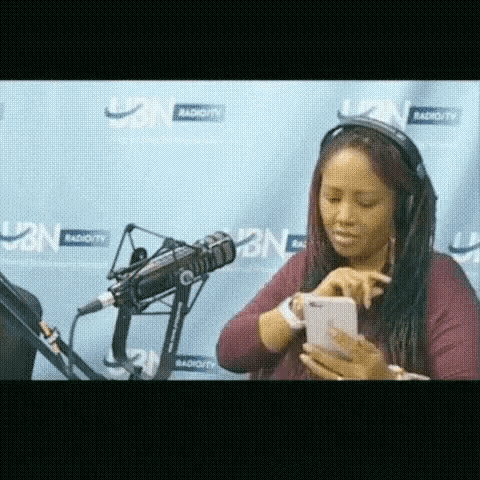 a woman wearing headphones looks at her phone in front of a radio station
