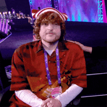 a man wearing a red shirt and a lanyard that says ' spongebob ' on it is sitting on a stage
