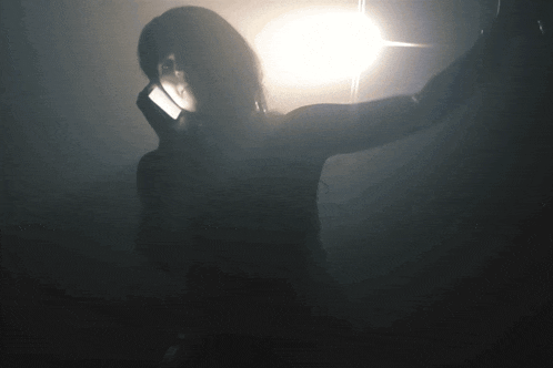a woman is standing in a dark room with a light shining on her