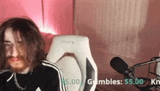 a man with long hair and a beard is sitting in a chair with a microphone in front of him .