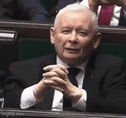 a man in a suit and tie is sitting in a parliament with his hands folded .