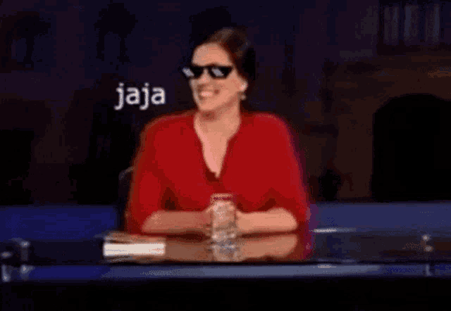 a woman wearing sunglasses and a red shirt is sitting at a desk .